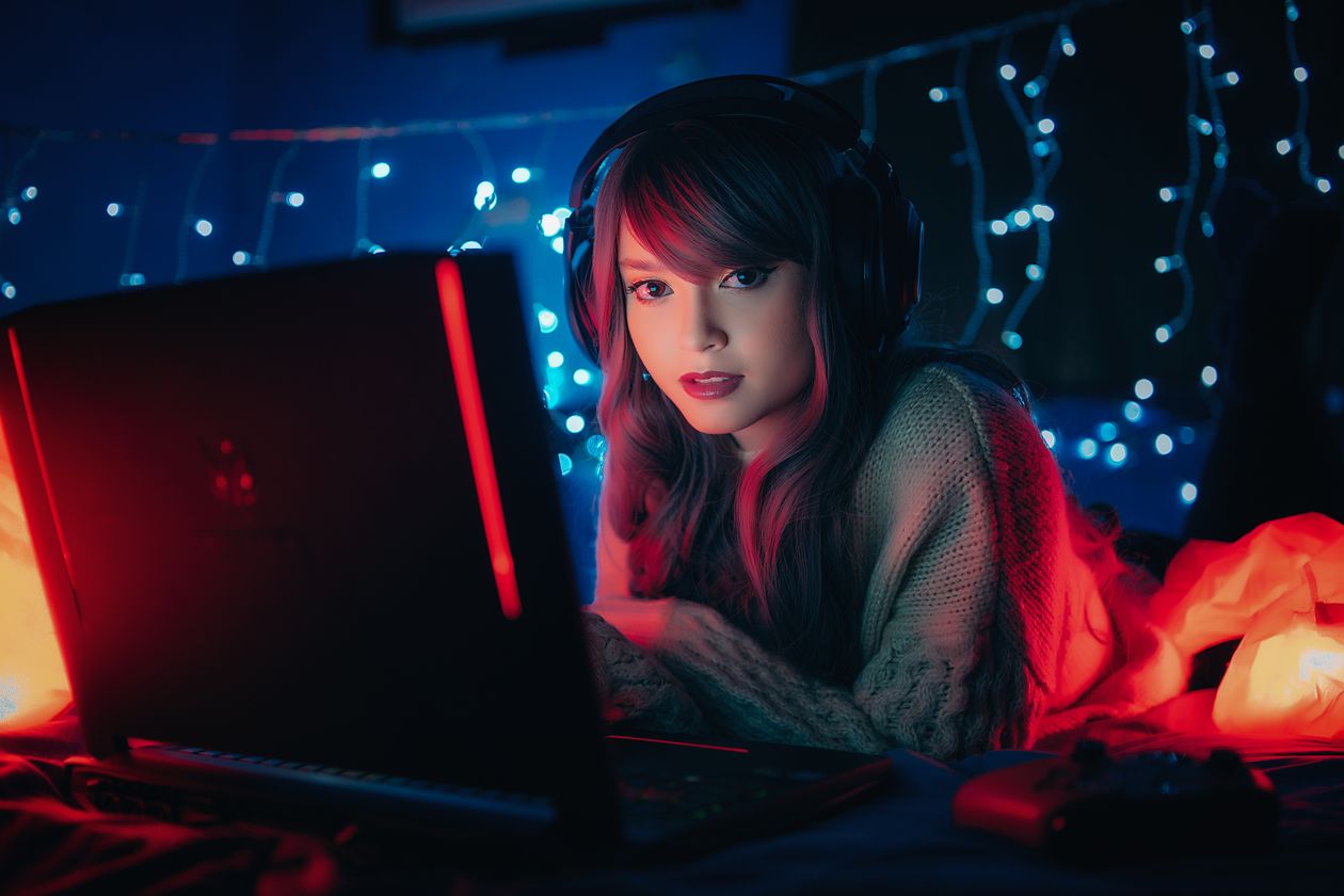 Person wearing headphones while gaming on a laptop at night Person wearing headphones while gaming on a laptop at night