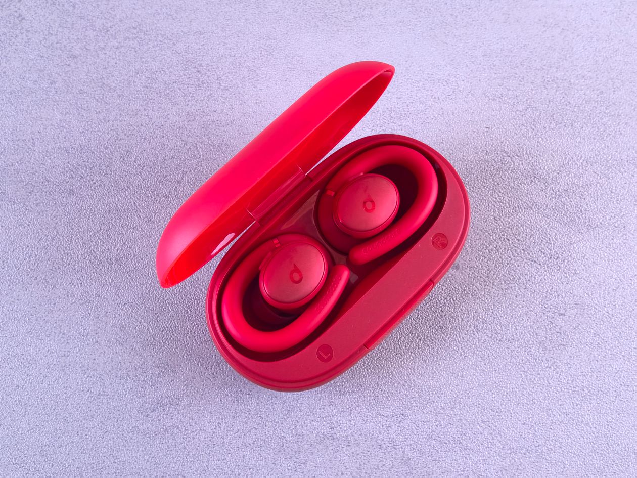 Wireless earbuds in a red charging case on a textured surface