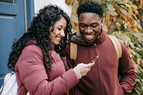 Two people looking at a smartphone screen together, similar to sharing camera access Two people looking at a smartphone screen together, similar to sharing camera access