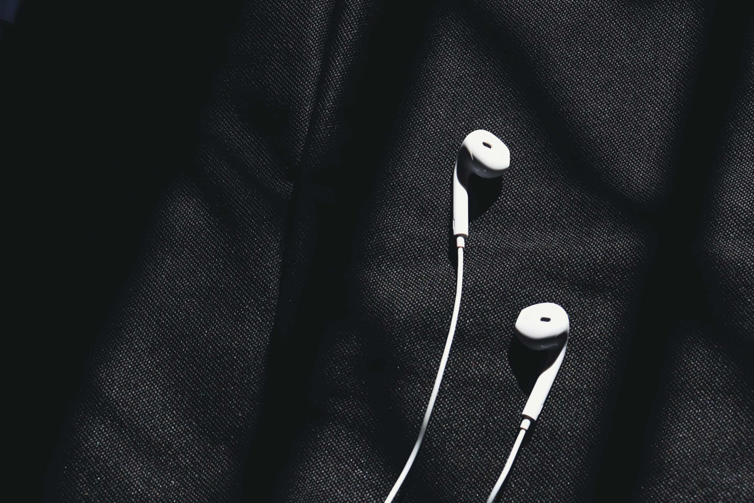 Close-up of wired in-ear earphones resting on dark fabric Close-up of wired in-ear earphones resting on dark fabric
