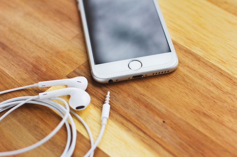 Wired earphones plugged into a phone headphone jack on a wooden desk Wired earphones plugged into a phone headphone jack on a wooden desk