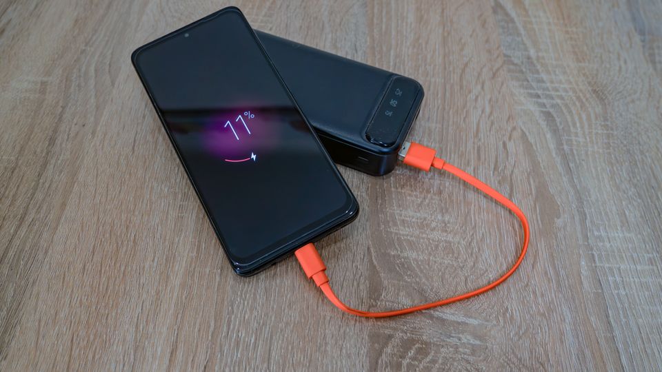 Smartphone charging from a power bank with cable on wooden table Smartphone charging from a power bank with cable on wooden table