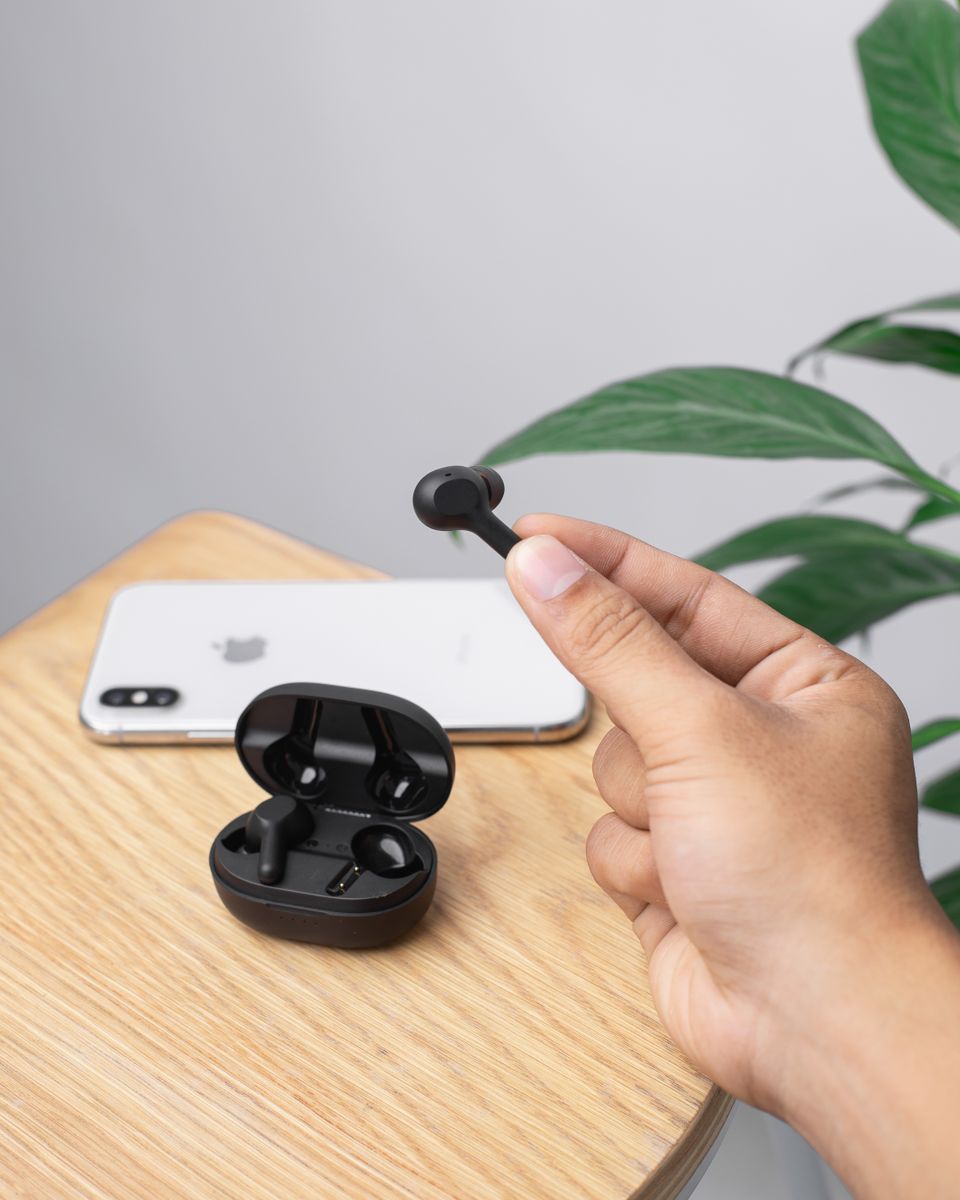 Hand holding black wireless earbuds next to a smartphone Hand holding black wireless earbuds next to a smartphone