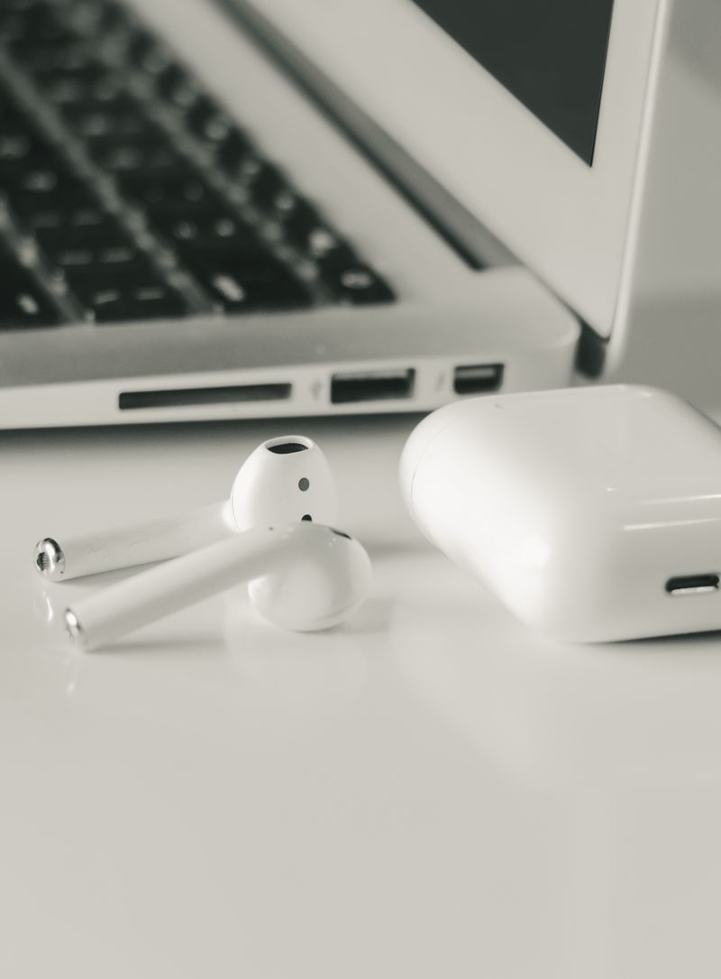 Small white wireless earbuds next to their charging case on a desk Small white wireless earbuds next to their charging case on a desk