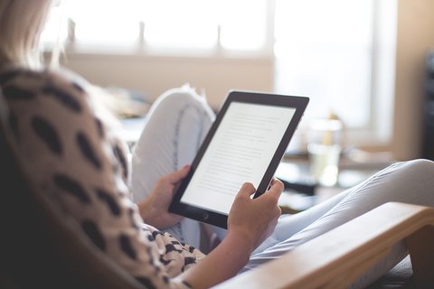 Person reading an e-book on a portable e-reader device Person reading an e-book on a portable e-reader device