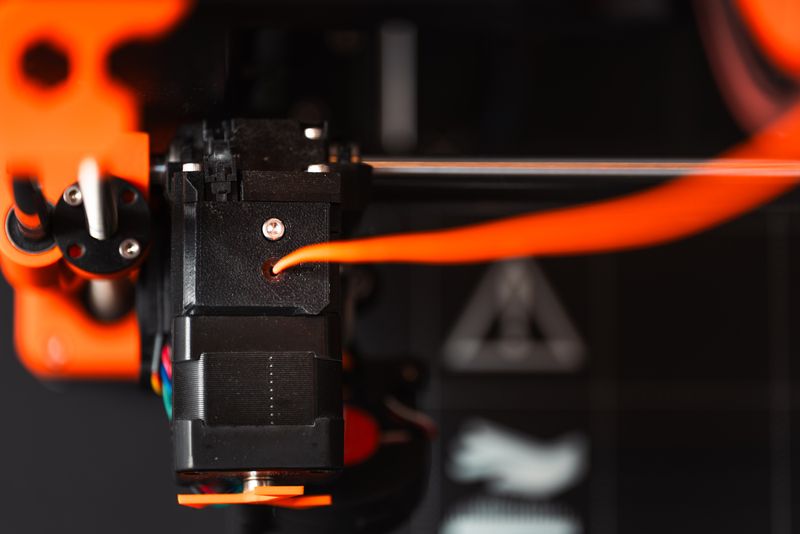 Close-up of 3D printer extruder nozzle extruding orange filament Close-up of 3D printer extruder nozzle extruding orange filament