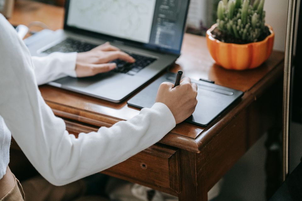 Person connecting a pen tablet to a laptop on a wooden desk setup Person connecting a pen tablet to a laptop on a wooden desk setup
