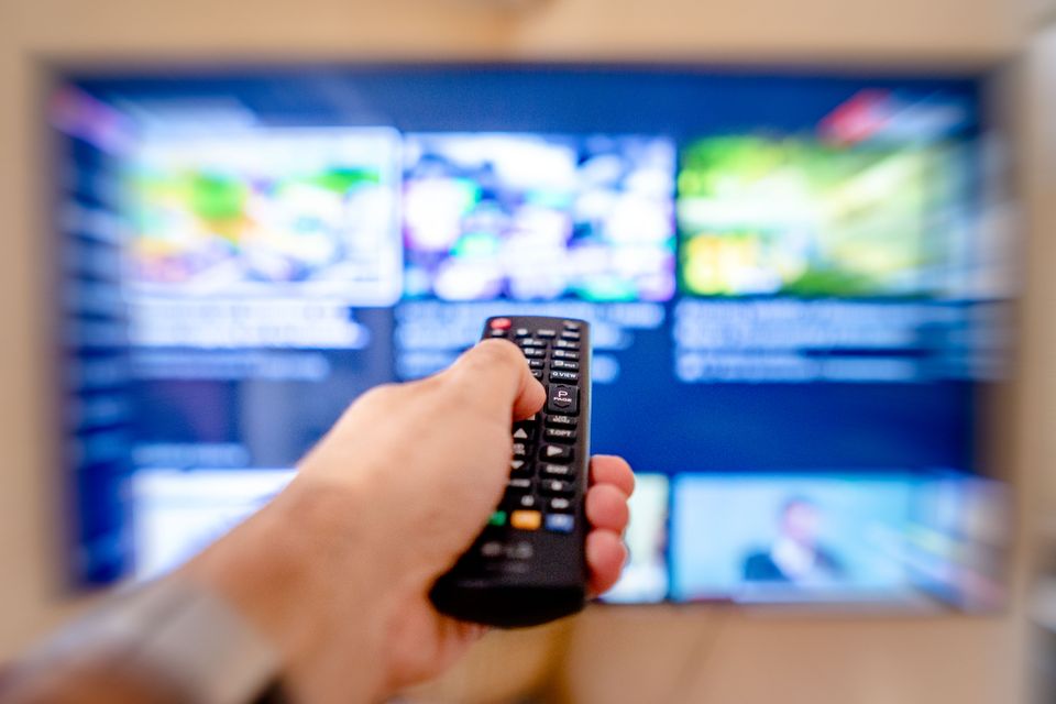 Hand pointing a TV remote control toward a television screen displaying channels Hand pointing a TV remote control toward a television screen displaying channels