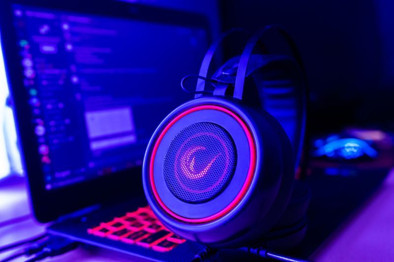 RGB gaming headset glowing red next to a laptop screen RGB gaming headset glowing red next to a laptop screen
