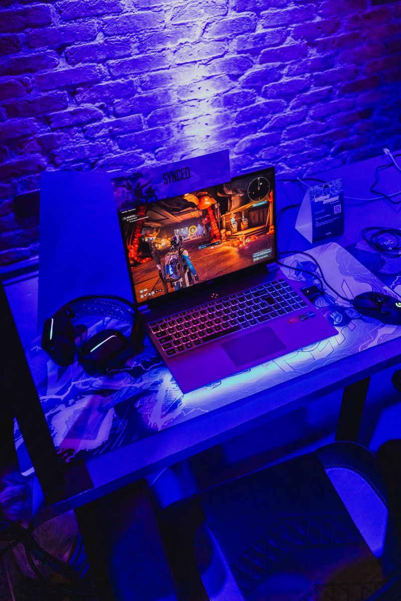 Gaming headset resting beside a laptop under purple neon lighting Gaming headset resting beside a laptop under purple neon lighting