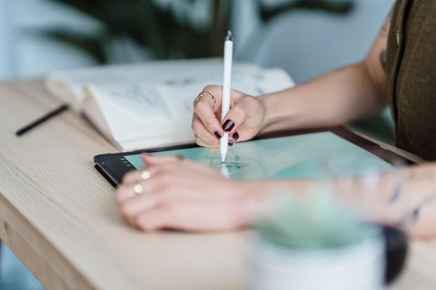 Close-up of a stylus pen tip pressed against a tablet surface with ring visible on hand