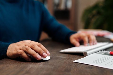 hand resting on a wireless mouse beside a keyboard on a desk hand resting on a wireless mouse beside a keyboard on a desk