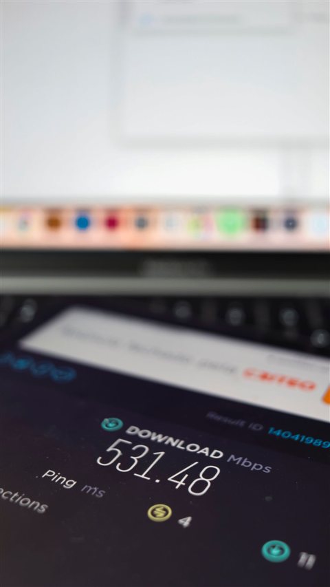 Smartphone displaying internet speed test results next to a laptop on a desk Smartphone displaying internet speed test results next to a laptop on a desk
