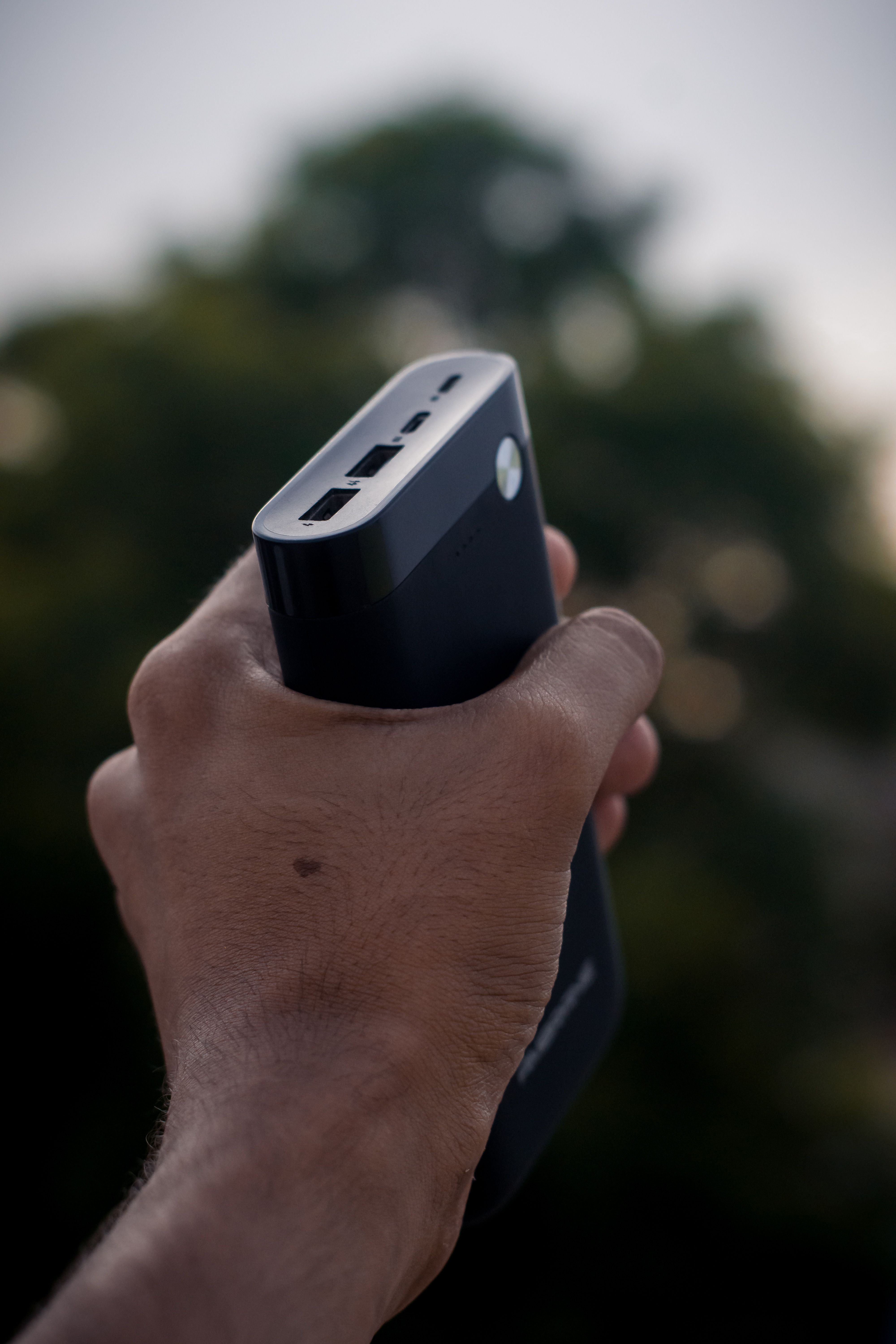 Hand holding a compact black power bank outdoors Hand holding a compact black power bank outdoors