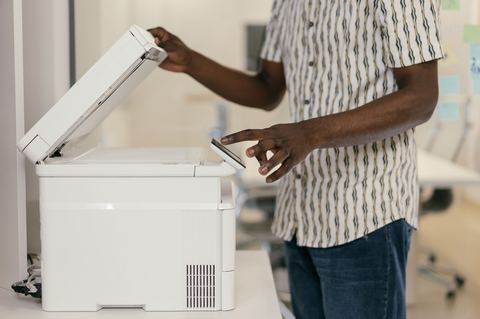 Person lifting the lid of a multifunction scanner in an office setting Person lifting the lid of a multifunction scanner in an office setting