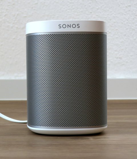 White and grey Sonos Play 1 wireless speaker standing on wooden table White and grey Sonos Play 1 wireless speaker standing on wooden table