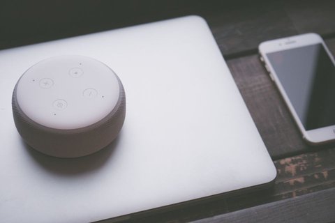 Small white smart speaker resting on laptop keyboard beside smartphone Small white smart speaker resting on laptop keyboard beside smartphone