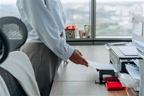 Office worker handing a printed page to a colleague near a shared printer setup Office worker handing a printed page to a colleague near a shared printer setup