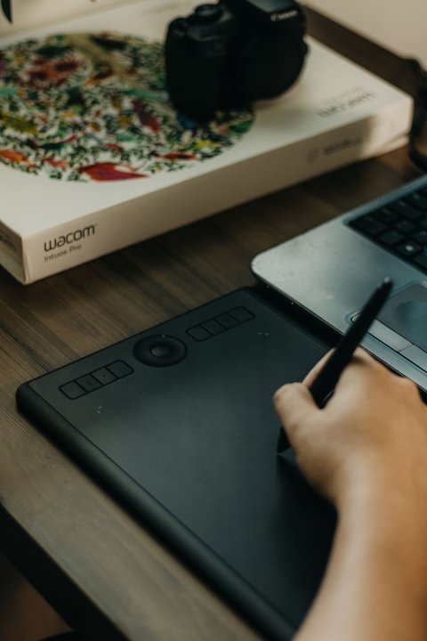 Wacom pen tablet box and tablet on a desk beside a laptop and camera Wacom pen tablet box and tablet on a desk beside a laptop and camera