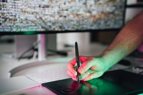 Hand gripping a stylus pen over a dark pen tablet surface near a keyboard Hand gripping a stylus pen over a dark pen tablet surface near a keyboard