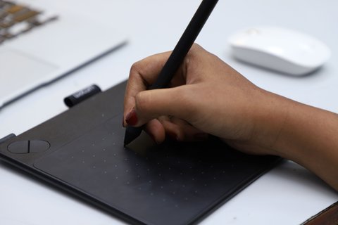Close up of a hand holding a stylus pen on a Wacom pen tablet surface Close up of a hand holding a stylus pen on a Wacom pen tablet surface