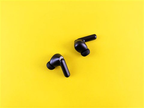 Pair of black true wireless earbuds resting on a bright surface Pair of black true wireless earbuds resting on a bright surface