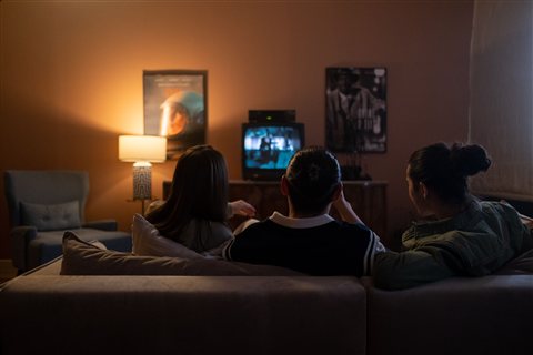 People sitting together on a couch watching a television screen in a dim room People sitting together on a couch watching a television screen in a dim room
