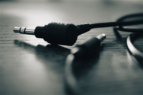 Two 3.5mm audio cable connectors resting side by side on a dark wooden surface Two 3.5mm audio cable connectors resting side by side on a dark wooden surface