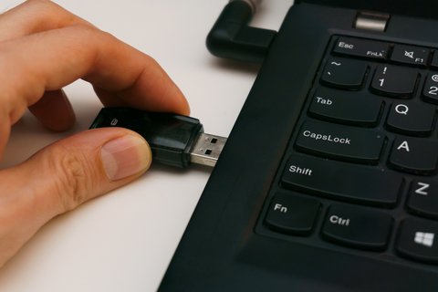 Hand plugging small USB Bluetooth adapter into laptop keyboard port Hand plugging small USB Bluetooth adapter into laptop keyboard port