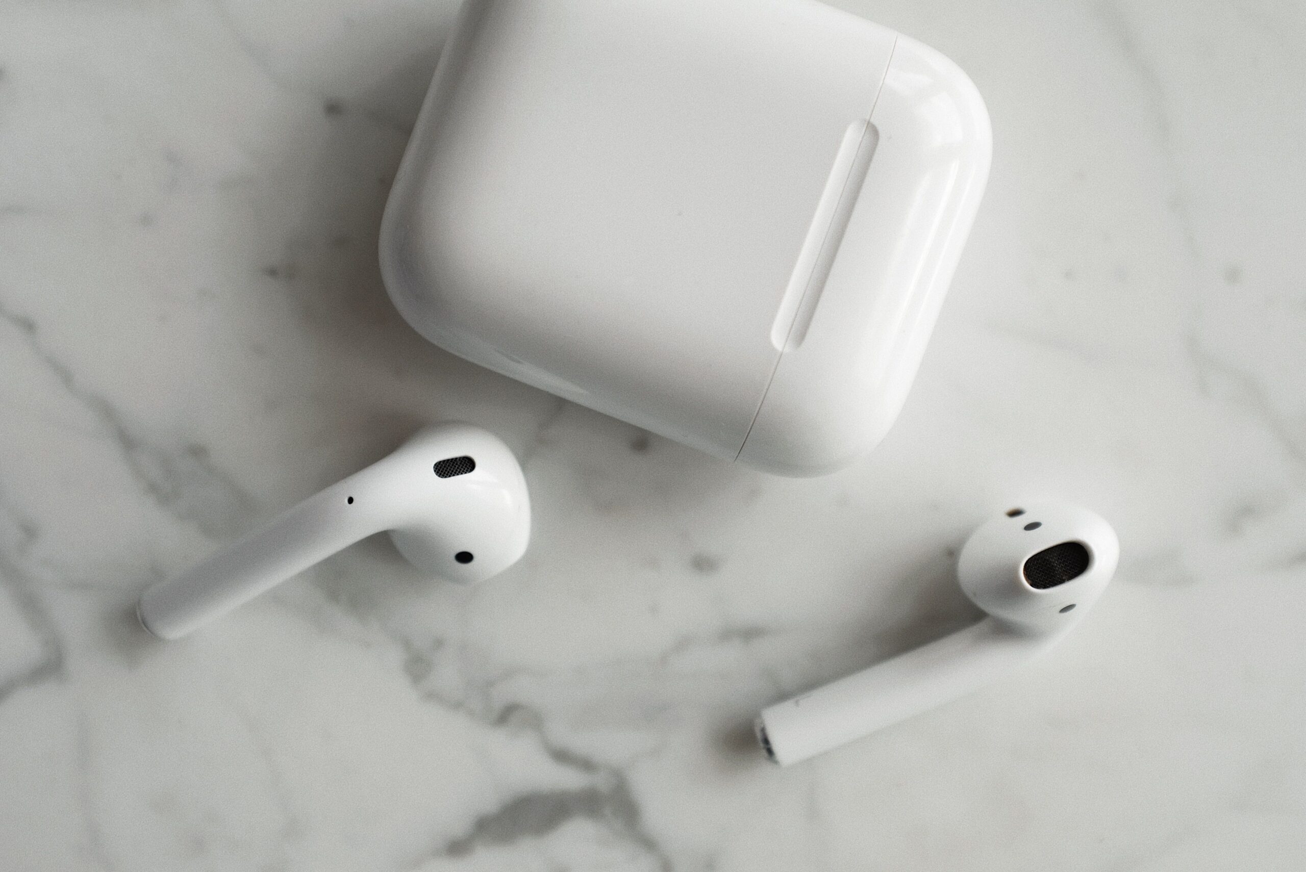 Compact true wireless earbuds resting beside their charging case Compact true wireless earbuds resting beside their charging case
