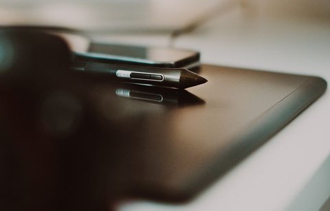 Hand holding a stylus above an orange portable hard drive cable and drawing tablet