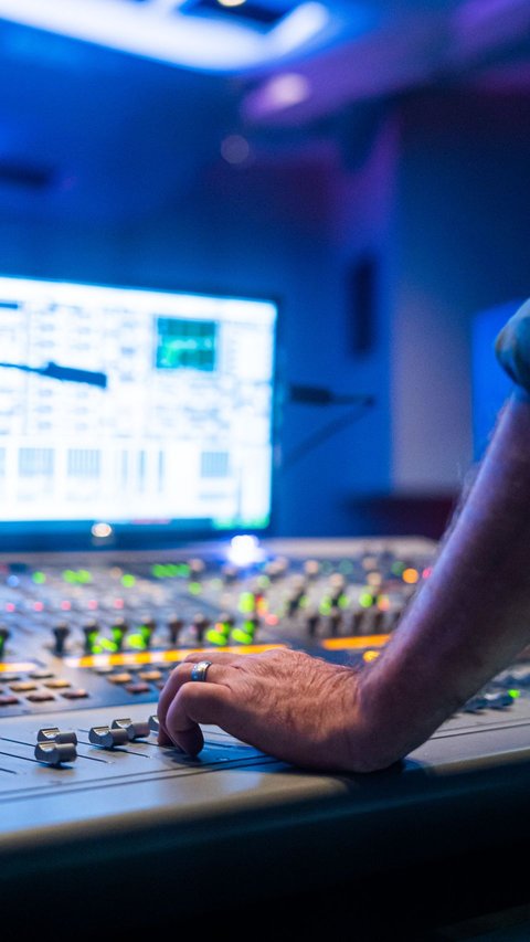 Sound engineer hand adjusting channel faders on a mixing console in studio