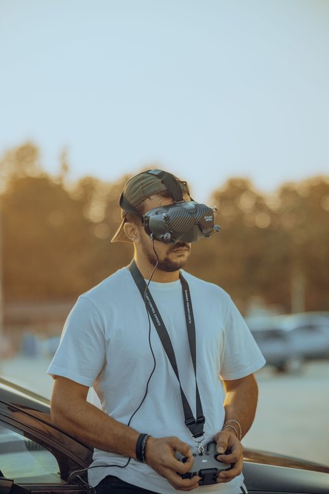 Pilot wearing DJI FPV Goggles V2 outdoors while holding the remote controller Pilot wearing DJI FPV Goggles V2 outdoors while holding the remote controller