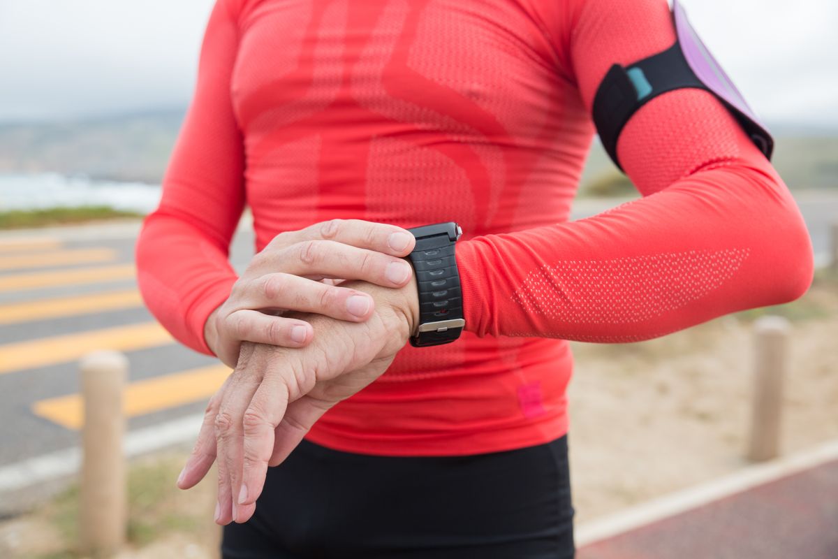 Runner checking a sport watch on the wrist while wearing red activewear outdoors Runner checking a sport watch on the wrist while wearing red activewear outdoors