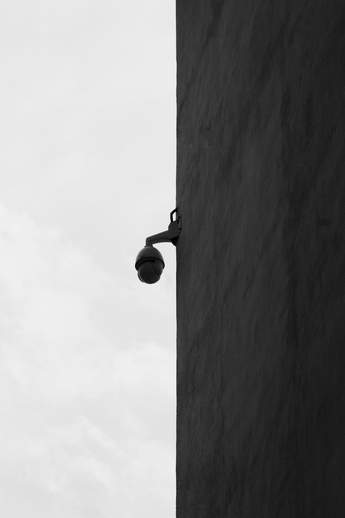 CCTV camera mounted on building corner against overcast sky silhouette