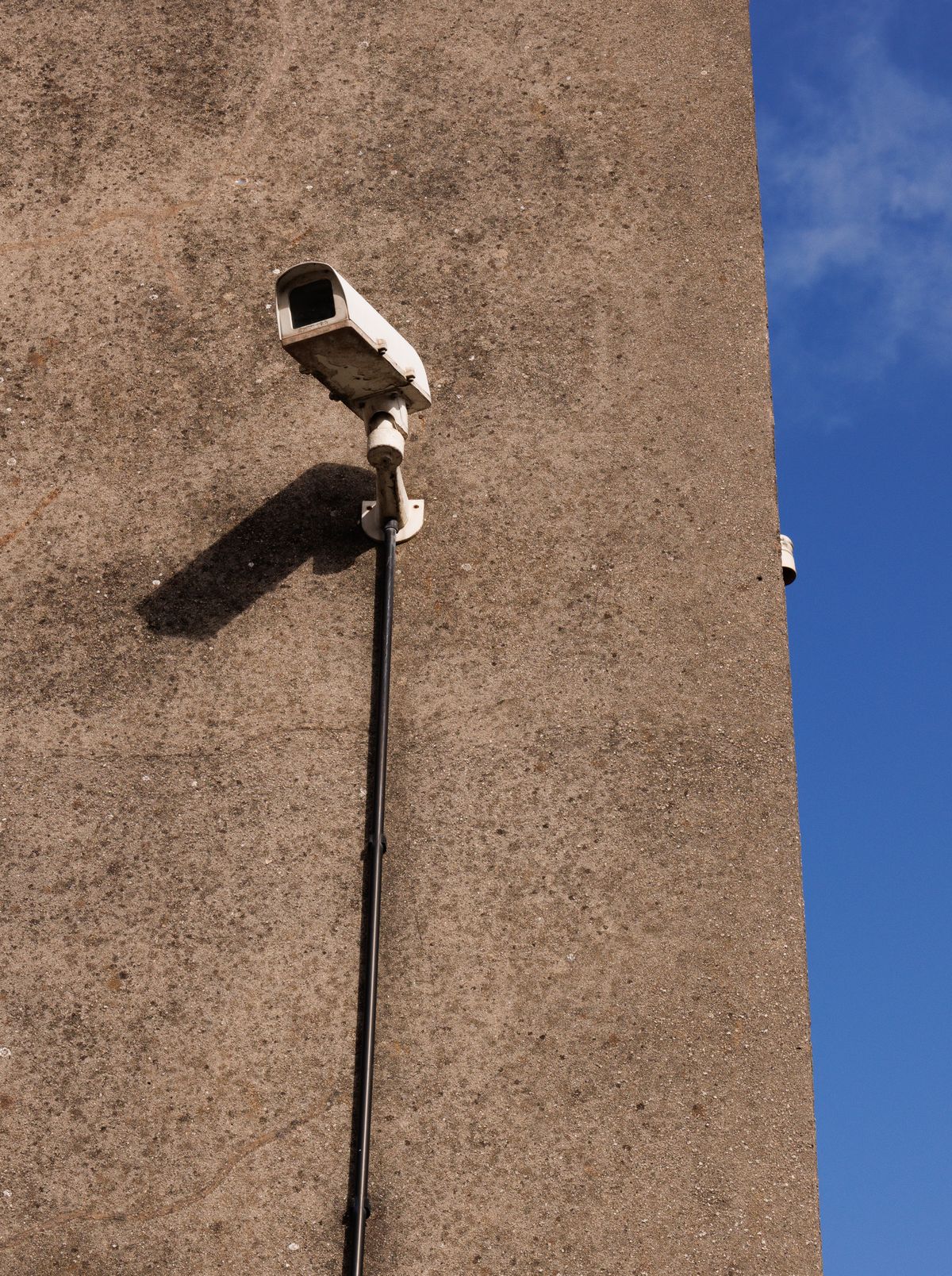 Outdoor security camera fixed on concrete wall under clear blue sky