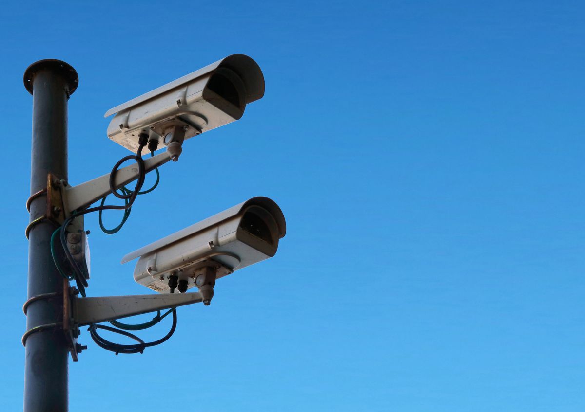 Two surveillance cameras mounted on a pole against a clear blue sky Two surveillance cameras mounted on a pole against a clear blue sky
