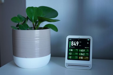Smart air quality monitor display showing real-time particle and humidity readings indoors Smart air quality monitor display showing real-time particle and humidity readings indoors