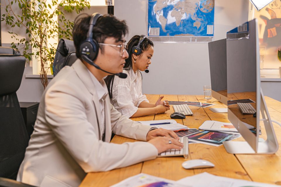 Two coworkers wearing wireless business headsets on a video call at their desks Two coworkers wearing wireless business headsets on a video call at their desks