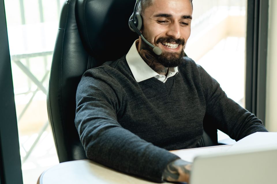 Man wearing an office headset smiling during a video call on his laptop Man wearing an office headset smiling during a video call on his laptop