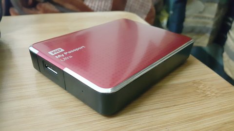 WD My Passport portable hard drive resting on a wooden desk near a laptop WD My Passport portable hard drive resting on a wooden desk near a laptop